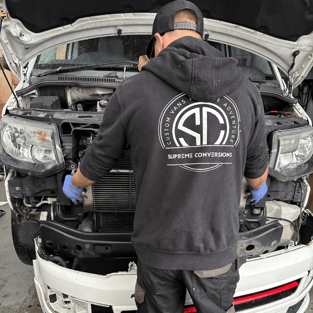 Technician repairing a car engine at Supreme Conversions workshop.